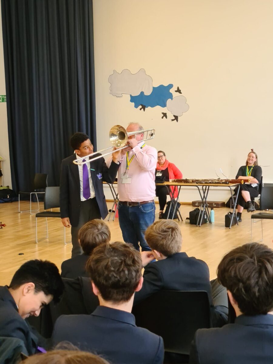 Staff playing musical instrument with a student stood next to them