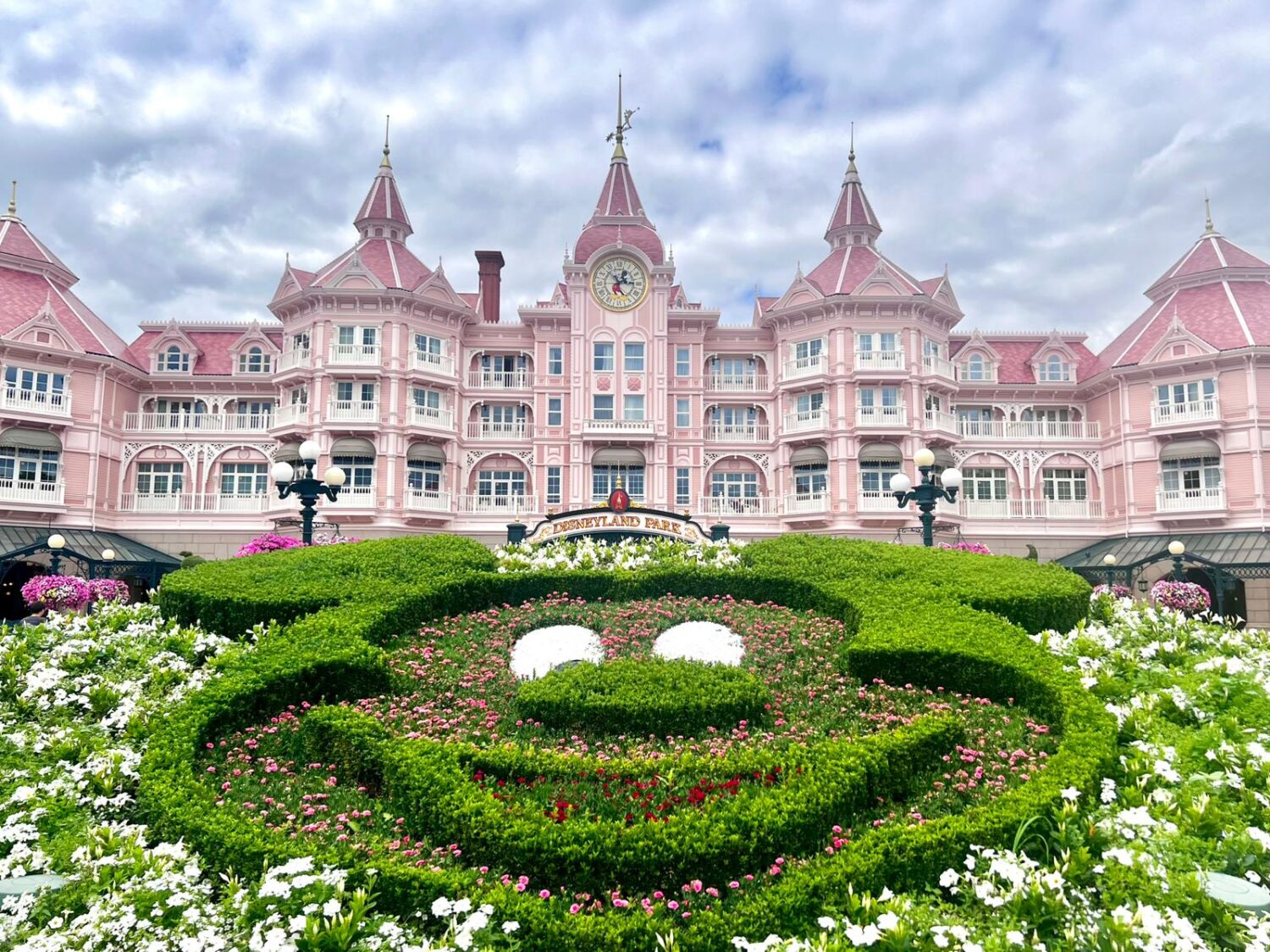 A picture of a hotel at disneyland with hedges in the foreground cut into the shape of mickey mouse