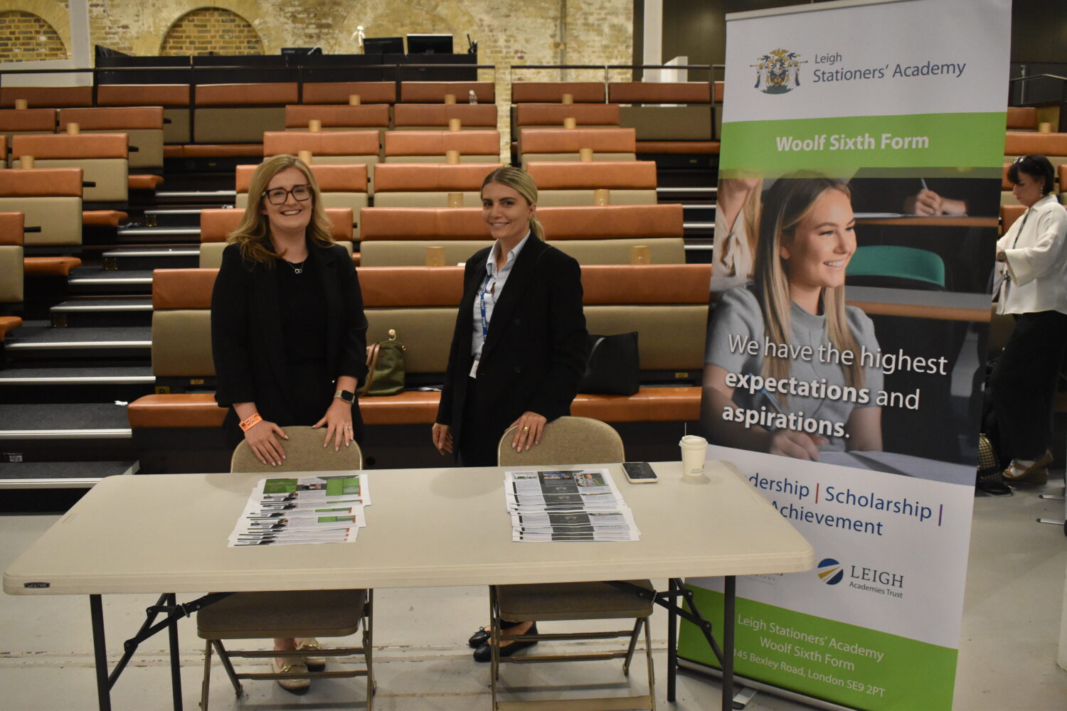 Based on the image, two women are standing behind a table at what appears to be an educational or recruitment event. The setting looks like a lecture hall or auditorium.