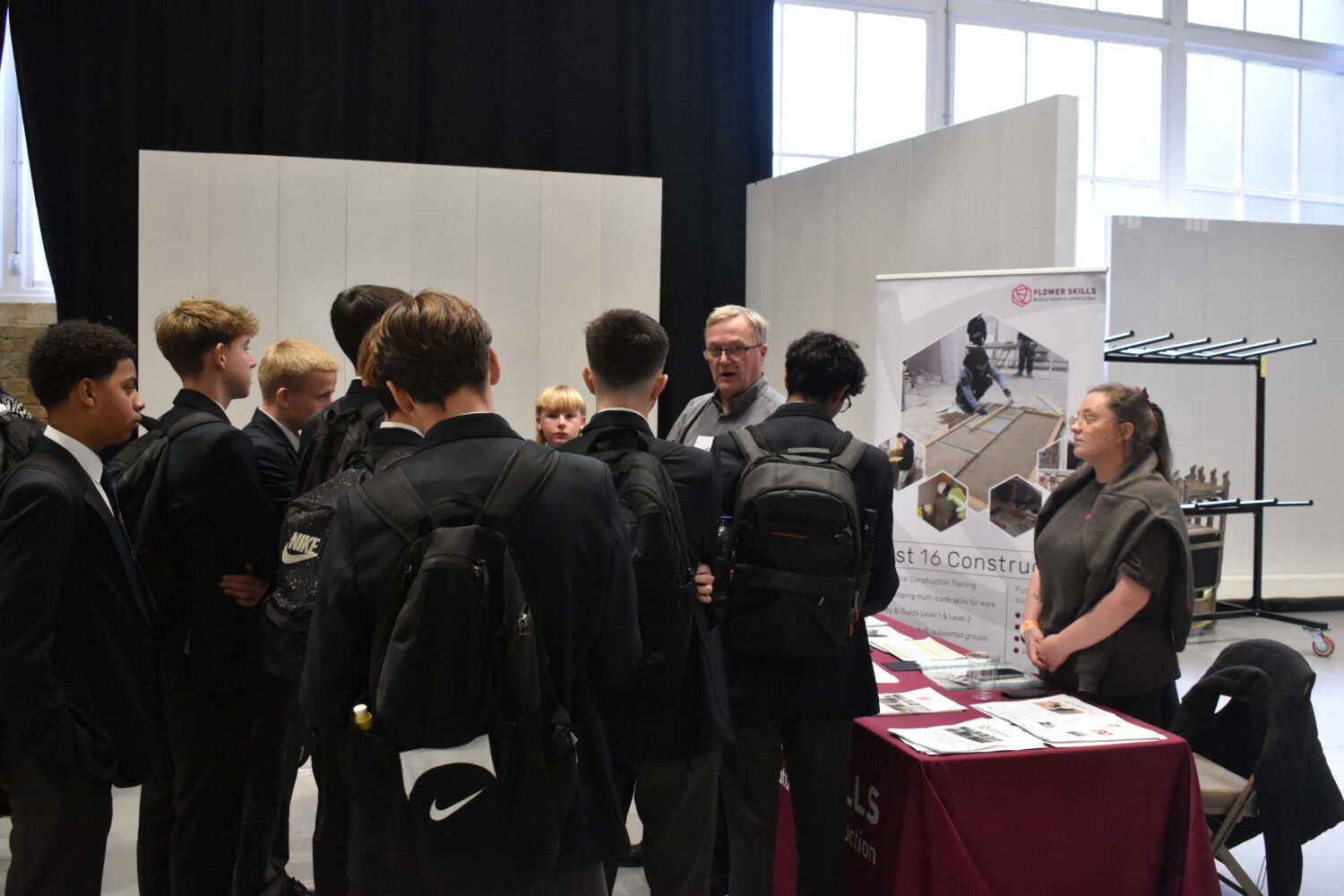 This photo shows students in school uniforms gathered around a man who is holding a flyer for "Construction Training Programmes." This suggests they are learning about different career paths and educational opportunities.