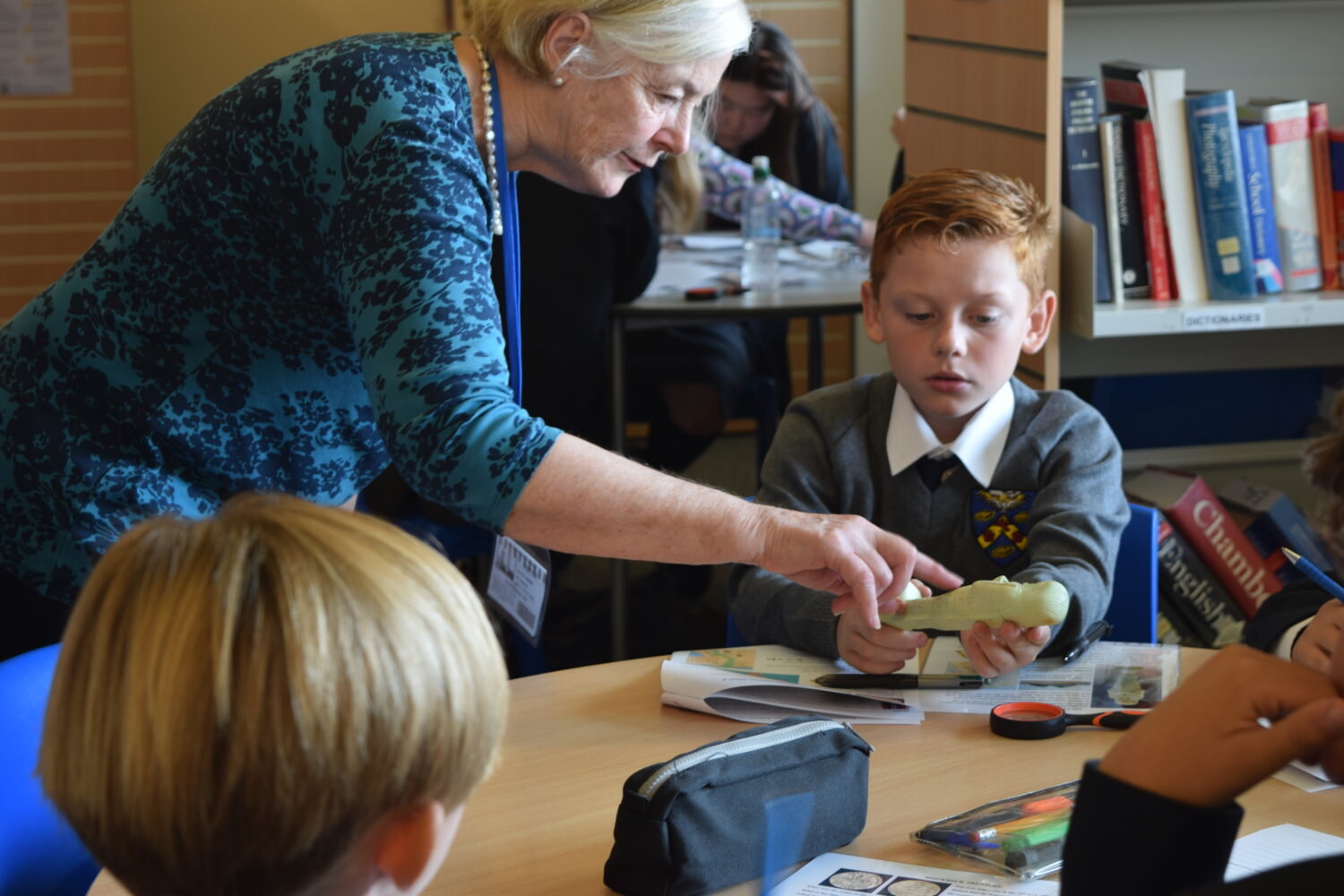 An adult, possibly a teacher or presenter, is interacting directly with the students. she is pointing to an object (a smooth, light-colored artifact) held by a student.