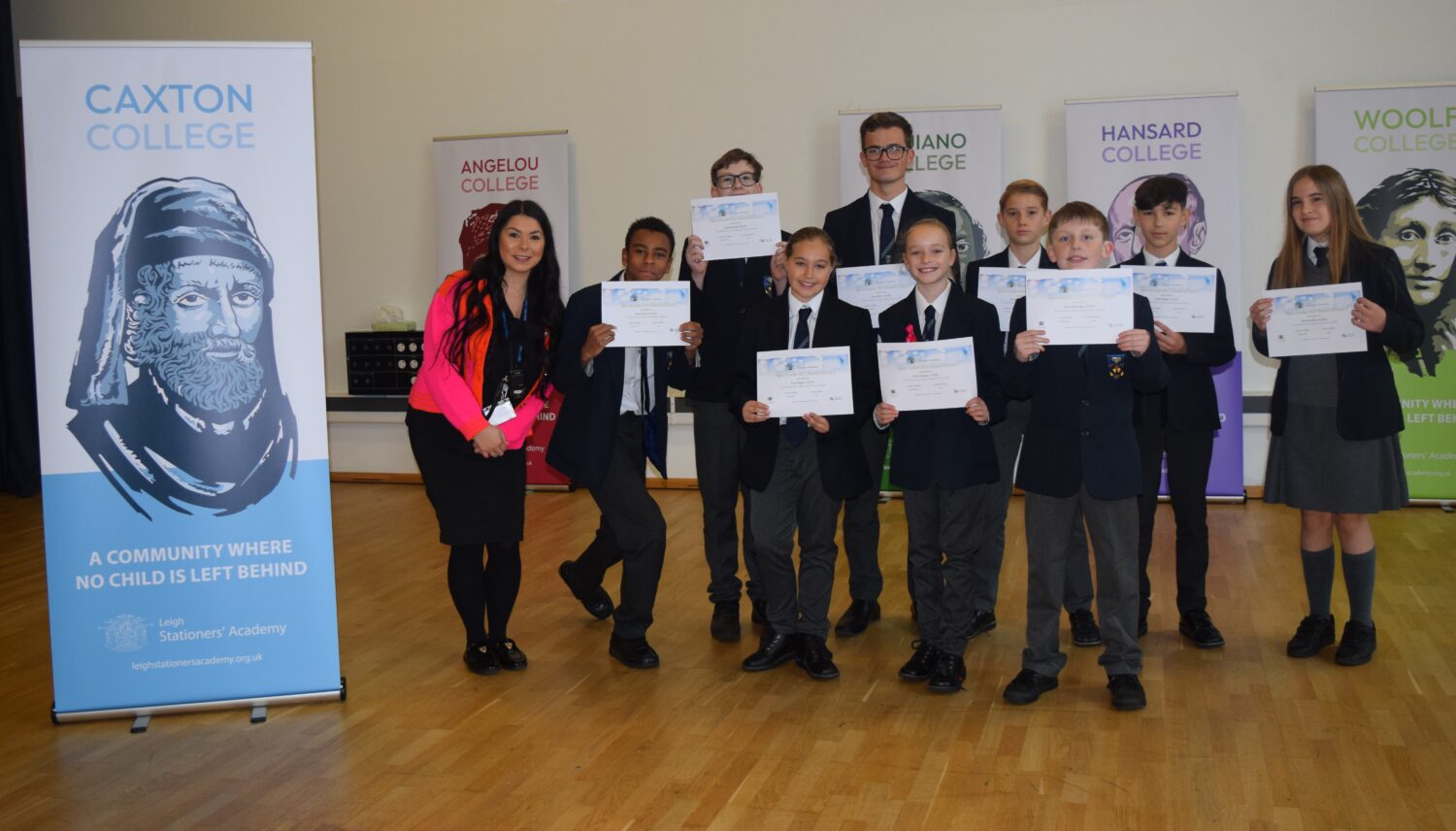This is a smaller group photo featuring students and one female staff member. The students are holding their certificates and posing in front of the college banners. The Caxton College banner is the most prominent one on the left.