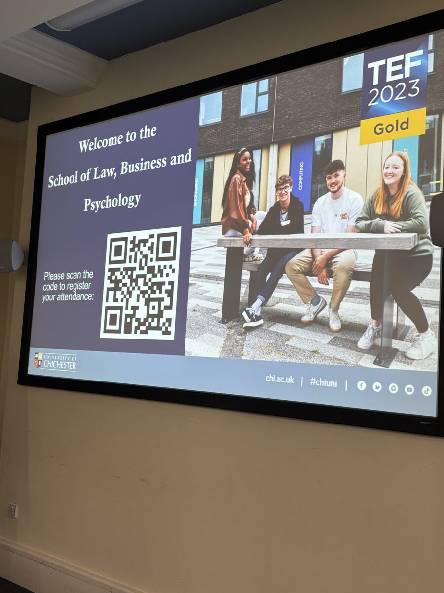 A projector screen displaying a "Welcome to the School of Law, Business and Psychology" slide with a QR code and University of Chichester branding.