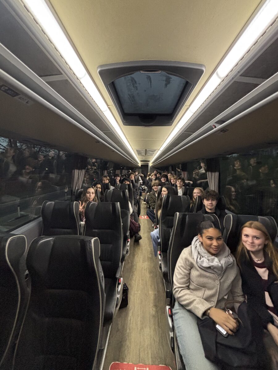 A view from the front of a coach bus looking down the aisle at rows of students seated and smiling during a trip.