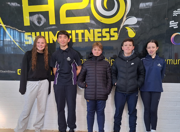 Students standing in front of a Swimming sign at a Swimming gala