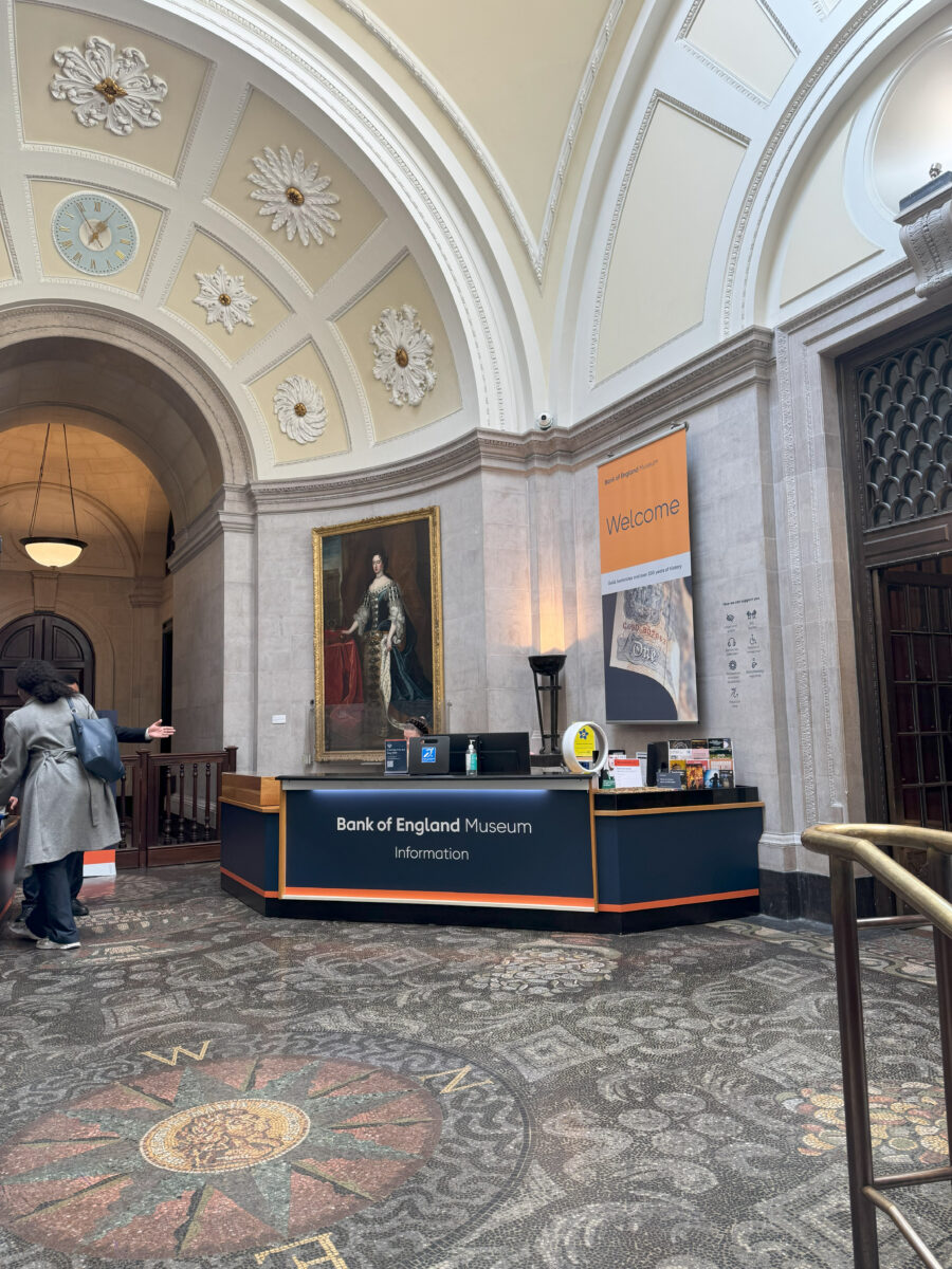 The museum's interior lobby featuring an ornate mosaic floor, a large portrait, and a modern "Welcome" information desk.