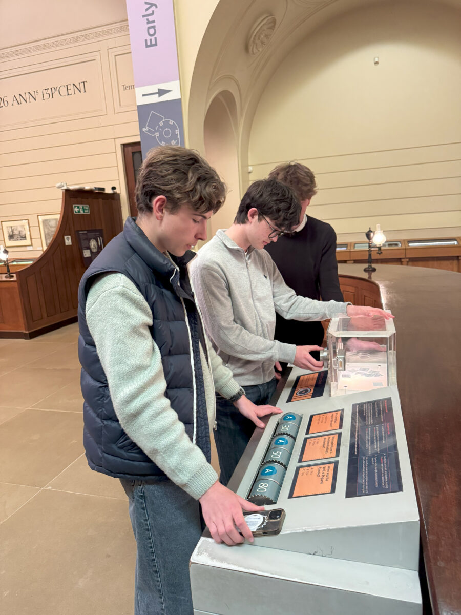Three students interact with a hands-on "Early" history exhibit featuring dials and a clear display case.