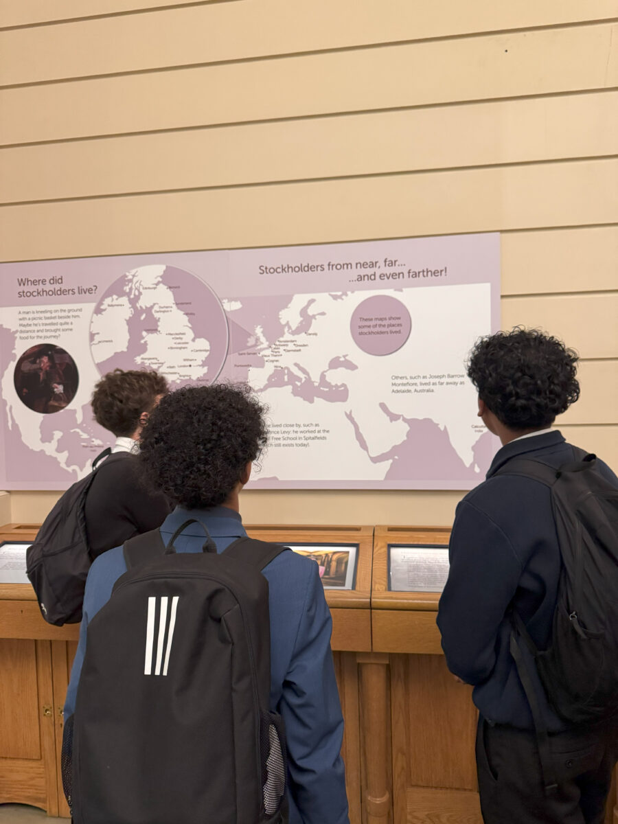 Three students stand with their backs to the camera, looking at a large map titled "Stockholders from near, far... and even farther!"