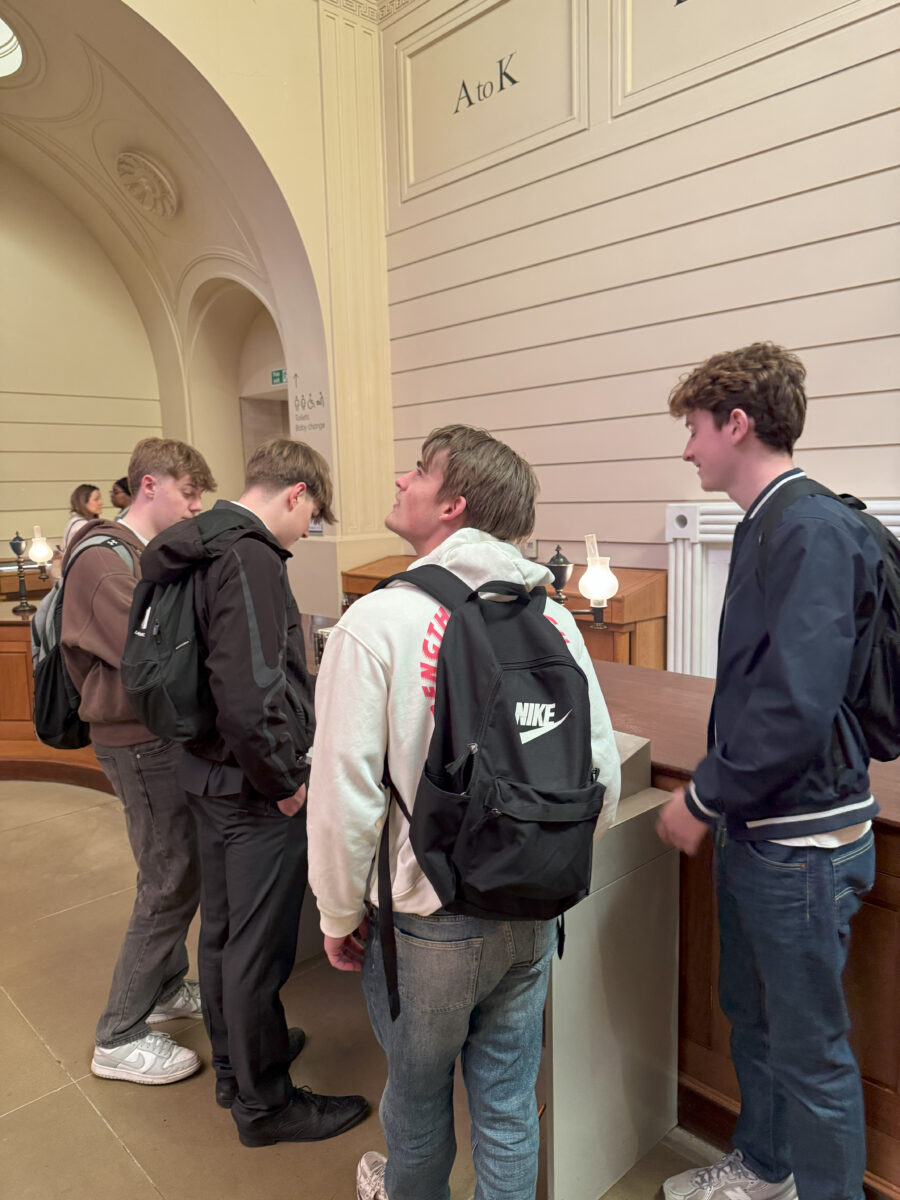 A group of students gathered around a museum display in a room marked with "A to K" signage on the wall.