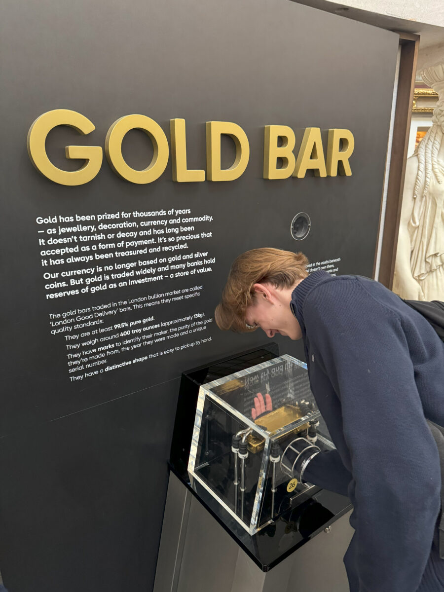 A student leans over a high-security display case to view a large gold bar, with informational text on the wall behind him.
