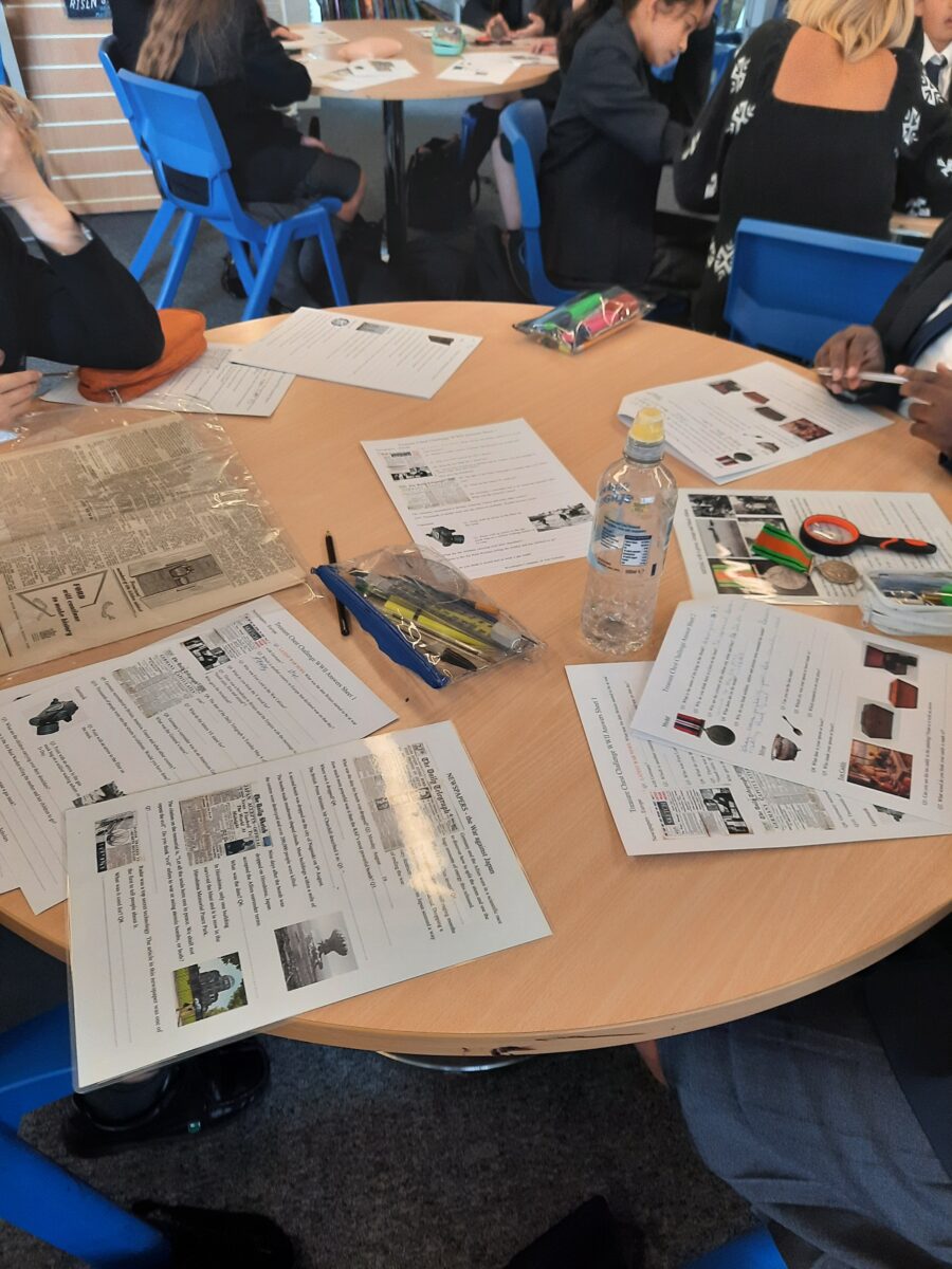 Students' worksheets, printed photographs and pens spread across a classroom table during a history activity.