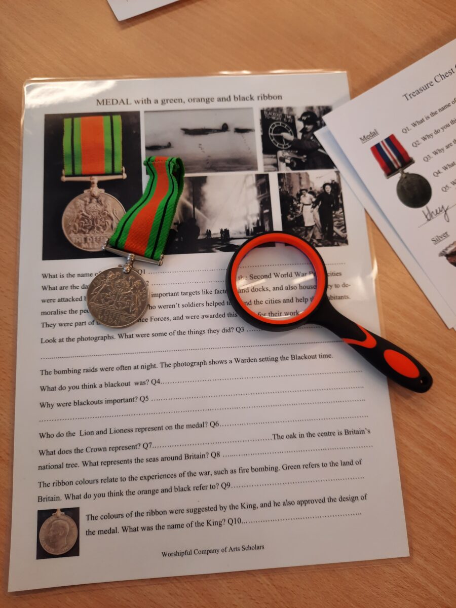 Two military medals with striped ribbons and a red-handled magnifying glass resting on printed sheets of historical photographs.