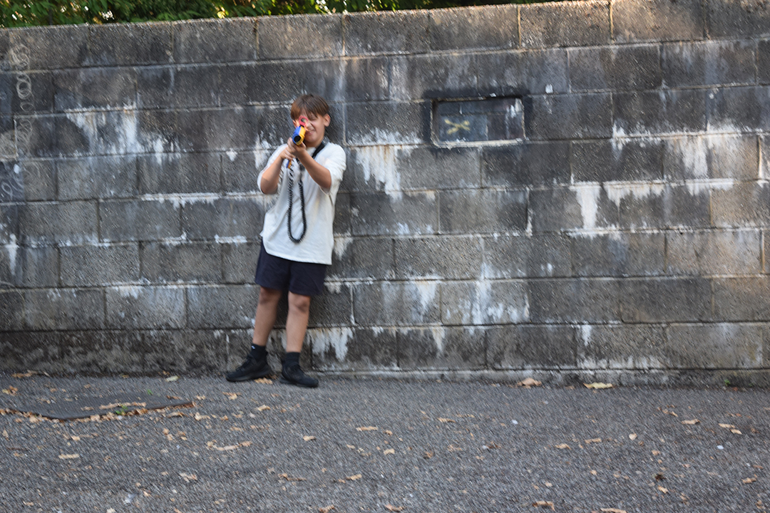 A child with a nerf gun by a brick wall